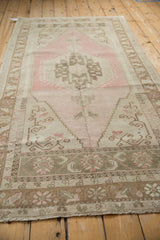 Angled view of a distressed Oushak rug with a soft, abrashed pink and beige ground.