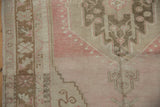 Time-softened texture and geometric motifs in blush pink and brown on a distressed vintage Oushak.