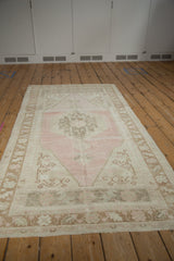 Angled view of a distressed Oushak rug showing its hexagonal pink medallion and beige abrashed ground.