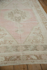 A low angle view of a distressed Oushak rug showing its soft texture and pink and beige hook motifs.