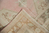 Corner of a vintage Oushak rug showing the hand-knotted back and distressed pink pile.