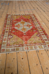 Distressed vintage Oushak rug corner, showing red, yellow, and ivory patterns with fringe.