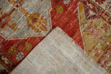 Distressed Oushak rug corner showing worn pomegranate red pile, exposed knot heads, and tightly woven foundation.