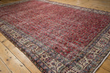 Distressed vintage Sparta carpet corner with textured cherry red vinery and beige floral border.