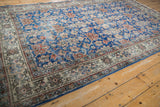 Distressed vintage Sparta carpet corner: blue field with floral motifs, worn ivory border.