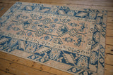 Distressed vintage Melas rug corner detail: dusty blush field with sapphire blue geometric patterns.