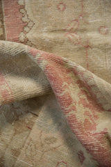 Folds revealing distressed texture of vintage Oushak rug in faded raspberry and beige.