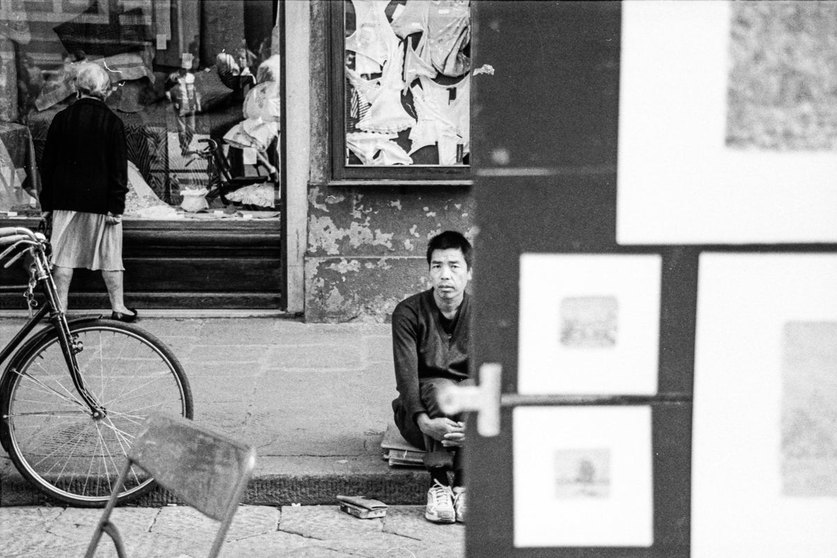 Black and white street photograph of a seated man looking directly at the camera.