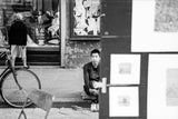 Black and white street photograph of a seated man looking directly at the camera.