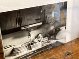 Plate, Pray, Play black and white art photograph of a kitchen still life with stacked plates and a small statue.