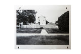 Black and white photograph of a house with a long wooden fence, yard, and sidewalk.