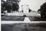 The stark geometry of a home, fence, and walkway in a black and white photograph.