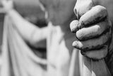 Black and white photograph showing a close-up of a weathered stone hand gripping a staff.