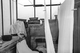 Monochromatic photograph of hanging linens, a chair, and textured architectural details.