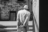 Man in a light suit and hat, seen from behind, contrasted with a graffiti wall in black and white.