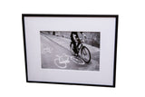 Framed black and white photograph, cyclist on road with bike symbols, 5x8 image.
