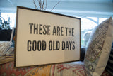 Distressed black 'These are the good old days' text on a vintage wooden sign.
