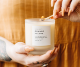 Hands lighting an Orange and Clove soy candle wick with a match.