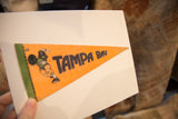 Creased orange and green vintage Tampa Bay felt pennant with player graphic, held by hand.