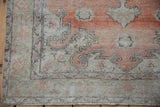 Distressed Oushak rug corner showing faded red, ivory leaf patterns, and fringed edge.