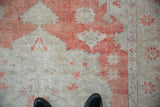 Distressed Oushak rug showing faded brick red, ivory, and visible knot heads.