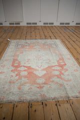 Distressed pile of the vintage Oushak rug with faded tomato red and antique ivory motifs.