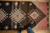 Distressed geometric medallion with hook motif in brown, blush pink, and ivory.