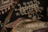 Textured hand-knotted pile with charcoal, brown, and blush geometric motifs, folded to show backing.