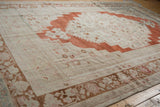Distressed Oushak rug corner showing abrashed madder red floral spandrel and vine border.