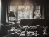 Sunlight streams through vertical blinds, creating deep shadows in a cluttered living room photograph.