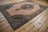 Angled view of a vintage Oushak carpet's dusty rose field, central medallion, and dark floral border.