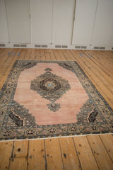 Full perspective view of a vintage distressed Oushak rug with a dusty blush field and dark scalloped medallion.