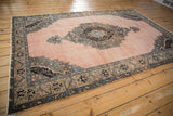 Angled view of a distressed Oushak carpet, highlighting its decorative medallion on a dusty rose field.