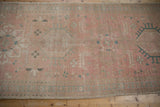 Distressed Karaja runner corner, faded pink field, blue geometric motifs, visible wear and faint foundation.