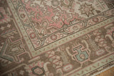Distressed vintage Tabriz rug corner with rose pink, pale green, and brown geometric motifs.