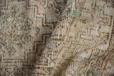 Worn distressed Oushak rug pile texture with beige, brown, and green geometric pattern.