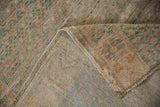 Distressed Oushak rug's dusty red and green pile, folded to reveal its woven backing and selvage.