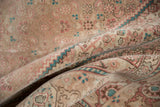 Folded vintage distressed Tabriz rug with muted beige, rose, and teal Herati patterns.