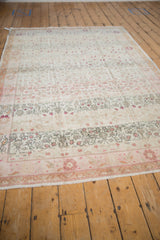 Distressed vintage Sivas carpet corner with dusty rose vinery, ivory field, and fringe.