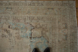 Distressed Tabriz rug corner, displaying ivory, blue, and brown millefleur motifs with fringe.