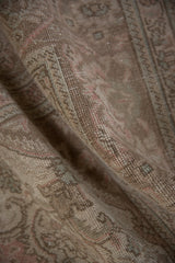 Distressed vintage Tabriz carpet showing worn pile and faded floral motifs in muted tones.