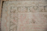 Distressed vintage Oushak rug corner, featuring pale pink, coffee brown, and ivory pile with intact selvage.