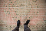 Distressed vintage Oushak rug texture, showing abrashed dusty rose field and green floral motifs.