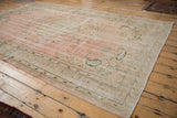 Distressed Oushak corner with pink field, green scrolled botehs, and secure selvage.