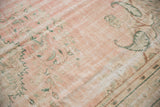 Distressed Oushak rug pile in dusty rose, faded green curvilinear patterns, showing wear.