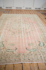 Faded rose and green border with visible wear and short fringe on the vintage Oushak rug.