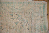 Distressed vintage Oushak carpet corner, faded peach and mint green geometric motifs.