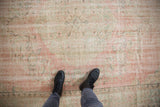 Distressed Oushak rug texture with faded blush, seafoam green, and ivory, viewed with black boots.