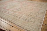 Vintage distressed Oushak carpet with worn texture and faded pink, green, ivory floral patterns.