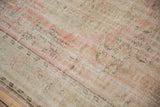 Distressed Oushak rug close-up revealing faded pink, green, and ivory floral patterns.